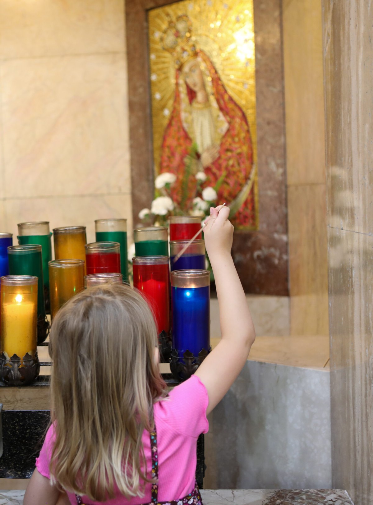 A young girl lights a votive candle